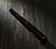The Franklin-Christoph Model 02 Intrinsic Black & Sweet Maroon pen lies diagonally on dark, rustic wood.