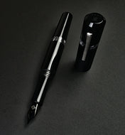 The Franklin-Christoph Model 19 Fountain Pen in Black & Dark Room Emulsion rests uncapped on a dark, textured surface.