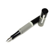 A Franklin-Christoph Model 19 Fountain Pen - GCB with a silver #6 nib and gray barrel rests next to its cap.