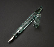 Franklin-Christoph Model 66 Septagonal Fountain Pen in Antique Glass rests on a dark surface, its silver nib gleaming.