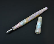 Franklin-Christoph Model 66 Septagonal Opal pen with marbled pastel finish rests beside its cap on a black surface.