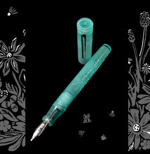 Load image into Gallery viewer, A translucent aqua fountain pen with floral engravings on the barrel, shown with its matching cap standing vertically in the background against a black backdrop with decorative white botanical illustrations.