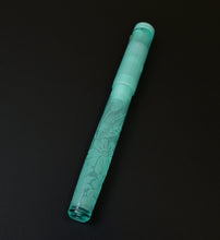 Load image into Gallery viewer, A translucent sea glass green glass fountain pen with etched floral patterns, shown diagonally on a solid black background.