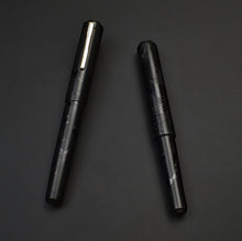 Load image into Gallery viewer, Two Franklin-Christoph Model 40 M Black Pen Society fountain pens with leaf engravings rest on a dark background.