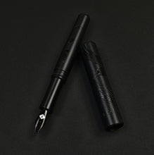 Load image into Gallery viewer, A Franklin-Christoph Model 40 M Black Pen Society fountain pen with Delrin matte finish rests uncapped on a dark surface.