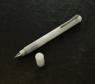 A Franklin-Christoph Model 25 Eclipse Fountain Pen - Ghost, uncapped, rests on a dark textured surface.