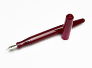 A Franklin-Christoph Model 65 Stabilis Fountain Pen in Sweet Maroon, uncapped, rests on a white surface.