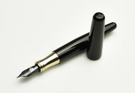 The Franklin-Christoph Pocket 66 FP - Black & Brass SE lies uncapped on a white surface, its gold trim gleaming.