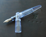 A Franklin-Christoph Pocket 66 Fountain Pen - Italian Ice, uncapped, rests on a black surface embossed with an ornate F.